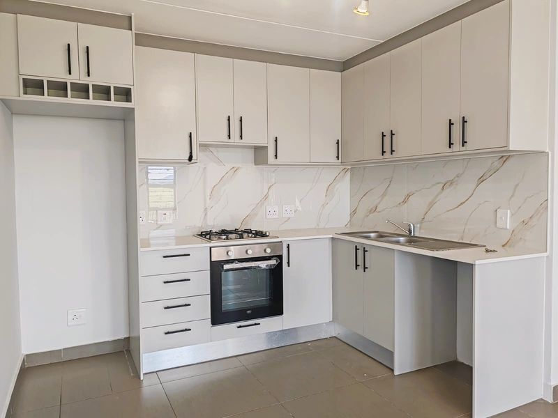 Modern kitchen featuring light grey cabinetry, stone countertops, marble-look splashback, built-in gas hob, and oven, with space for a refrigerator.