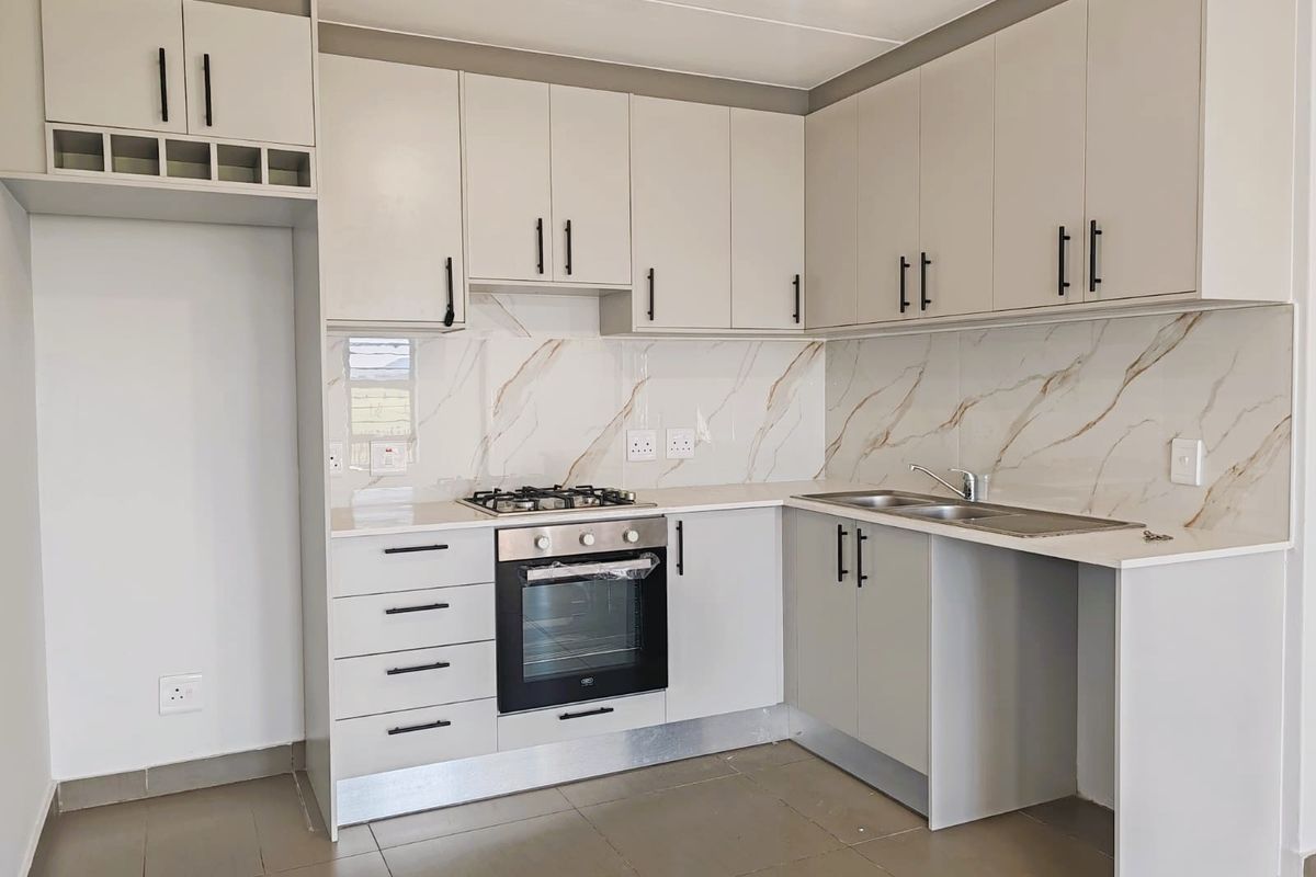 Modern kitchen featuring light grey cabinetry, stone countertops, marble-look splashback, built-in gas hob, and oven, with space for a refrigerator.