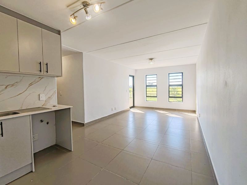 Bright open-plan living area featuring neutral tiled flooring, modern kitchen cabinetry with marble-effect splashback, and large windows providing natural light.