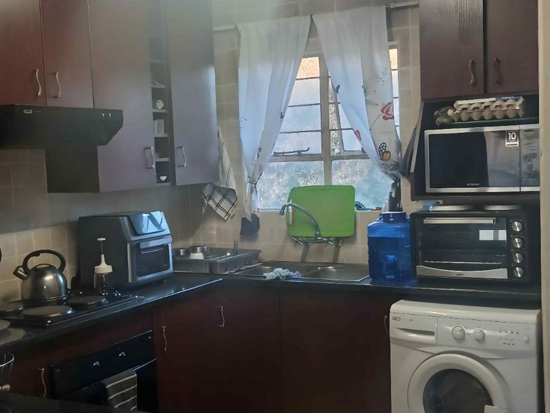 A functional kitchen featuring dark wood cabinetry, granite-look countertops, tiled backsplash, and integrated laundry plumbing for a washing machine.