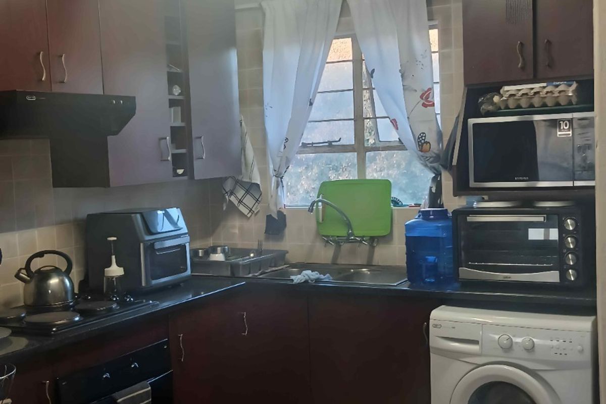 A functional kitchen featuring dark wood cabinetry, granite-look countertops, tiled backsplash, and integrated laundry plumbing for a washing machine.