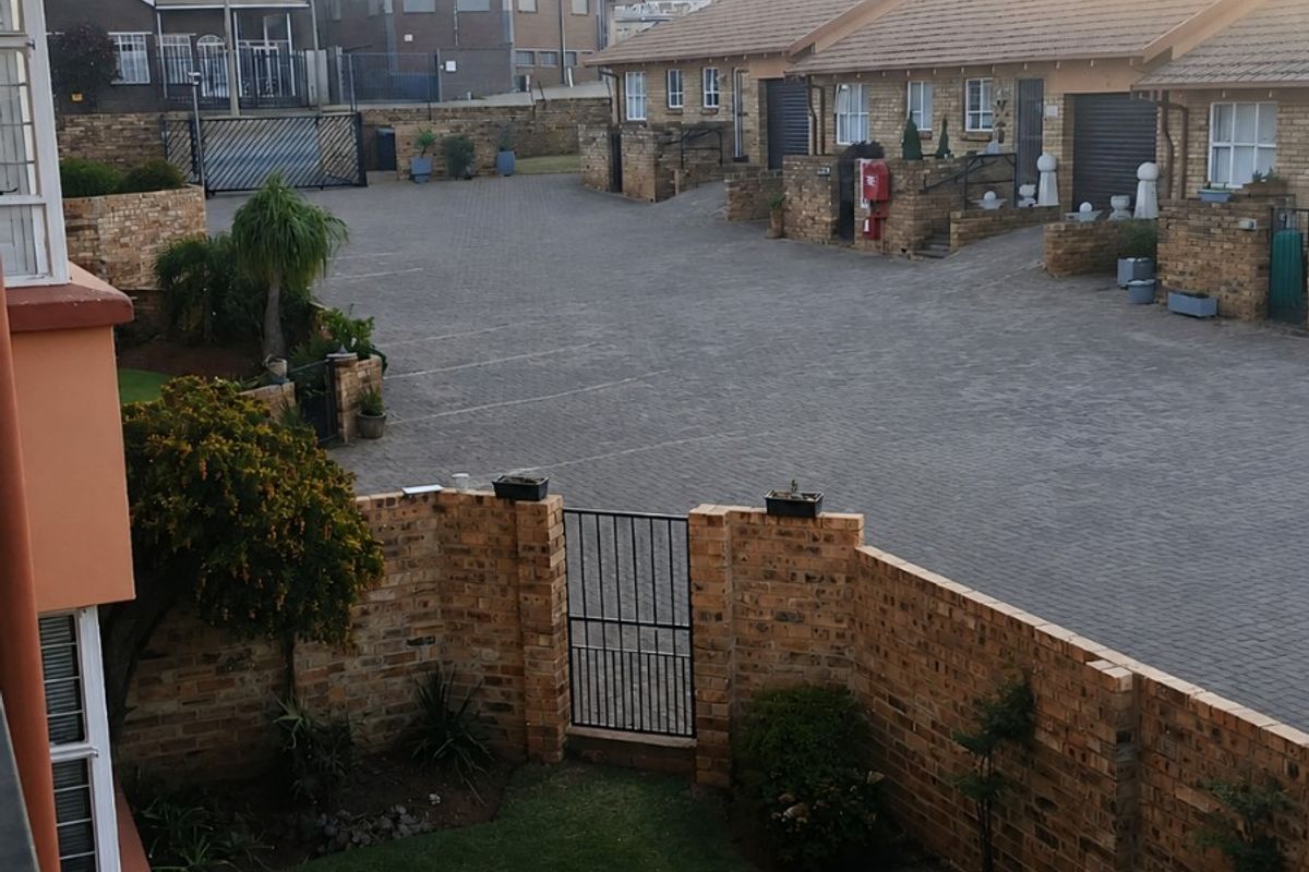 Elevated view of a residential complex courtyard featuring a private garden area, brick boundary walls, and paved communal driveway access.