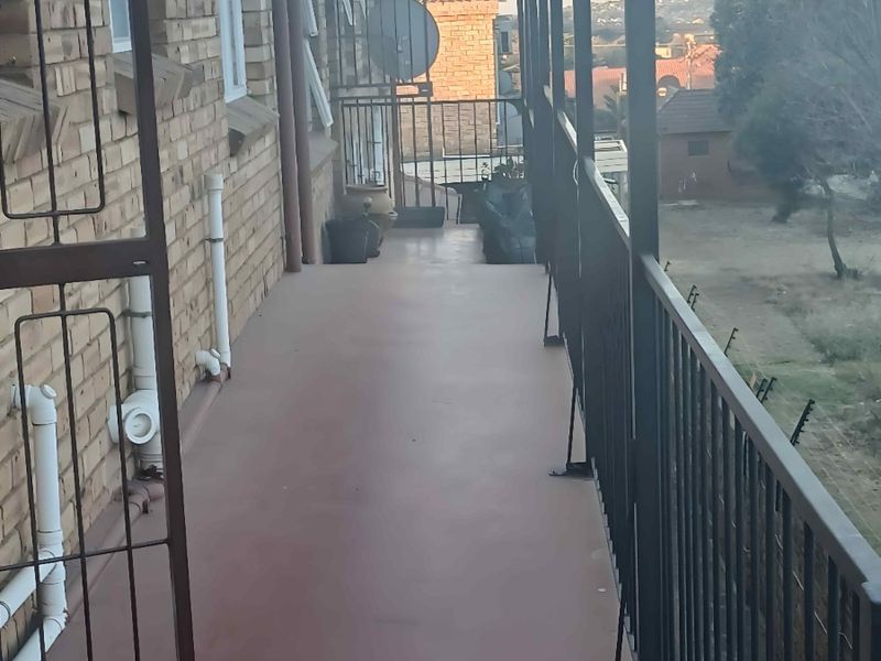 A long, narrow balcony featuring a brick facade, metal balustrade, and security gate, offering an elevated view of the surrounding neighbourhood.