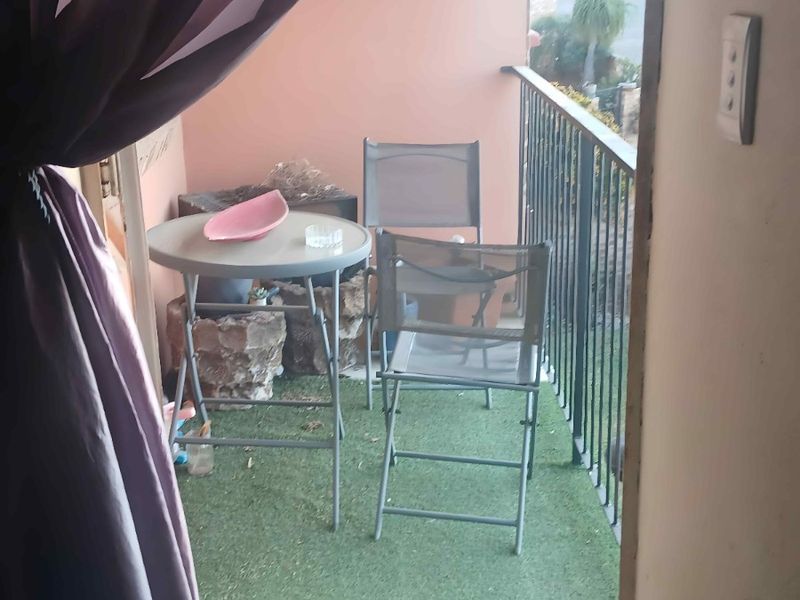A compact balcony featuring a metal safety railing and artificial grass flooring, providing a small outdoor space accessible from the interior.