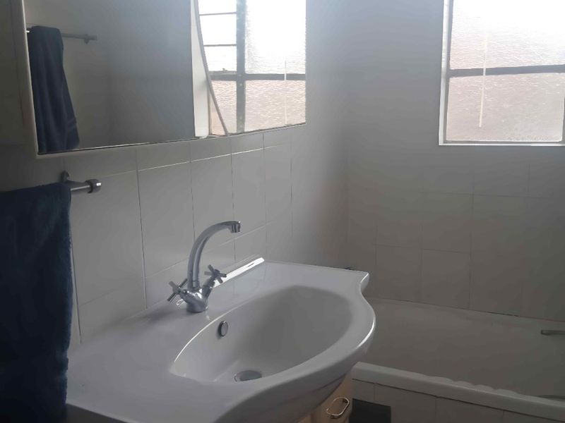 A functional bathroom featuring a vanity with basin, wall mirror, and a bathtub with tiled surround.