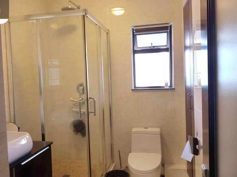 A modern bathroom featuring a glass-enclosed shower, a vessel sink vanity, a toilet, and neutral wall tiling with built-in storage.