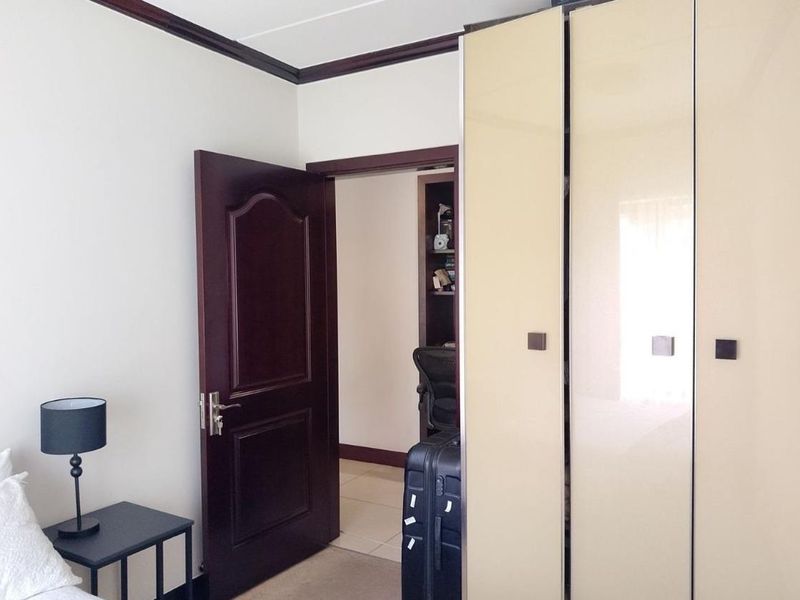 A bedroom featuring built-in cupboards with high-gloss finish, dark timber door, and crown molding, leading into an adjacent room.