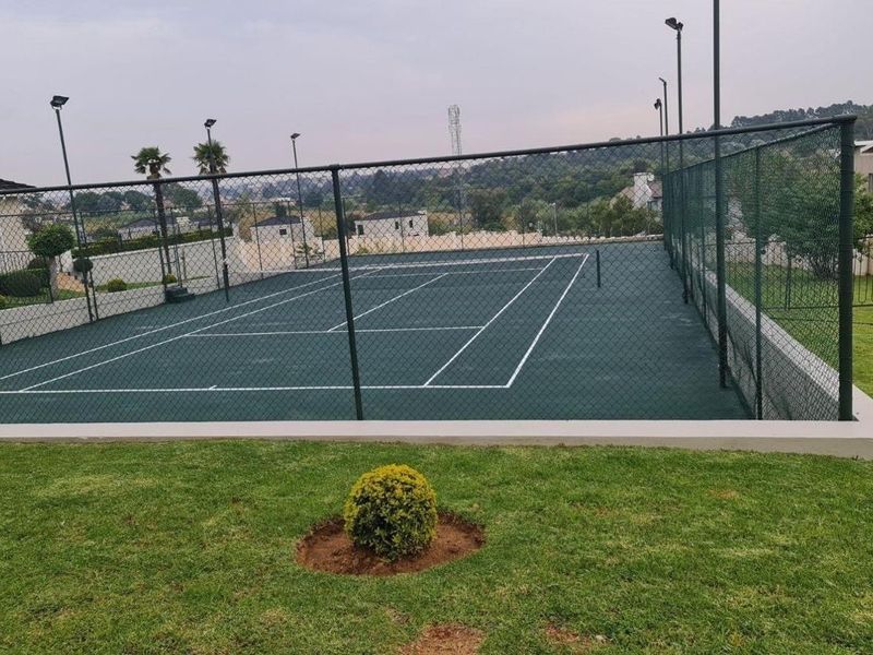 A well-maintained outdoor tennis court featuring a hard surface, perimeter chain-link fencing, and integrated floodlighting for evening play.