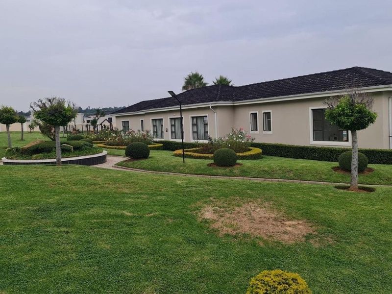 A view of the rear exterior of the apartment building, featuring a well-maintained landscaped garden, paved pathways, and a tiled roof.