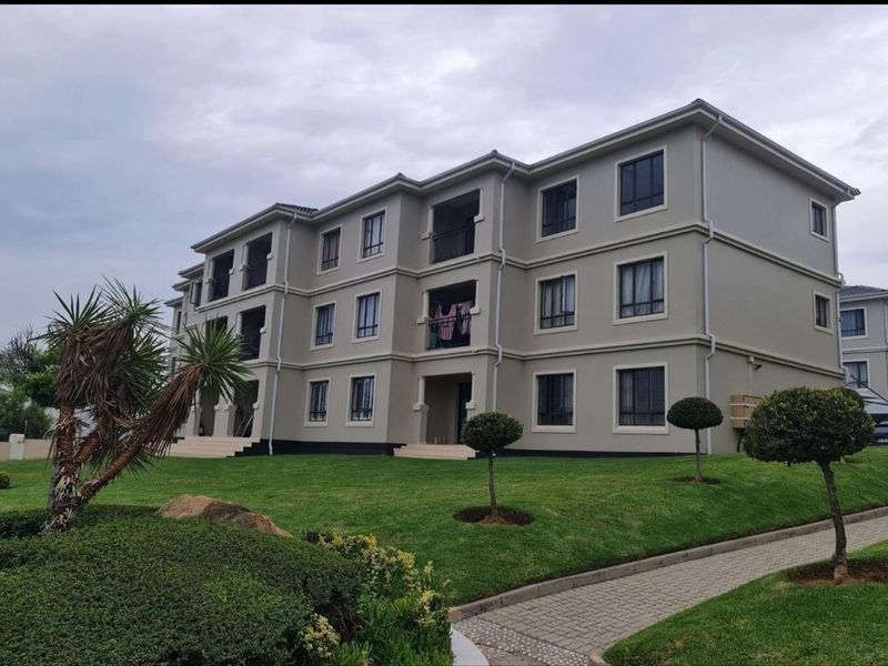 A multi-story apartment building featuring a well-maintained lawn, paved walkways, and private balconies with aluminum window frames.