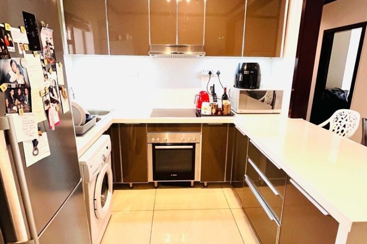 Modern kitchen featuring high-gloss cabinetry, stone countertops, integrated oven and hob, and tiled flooring with a functional U-shaped layout.