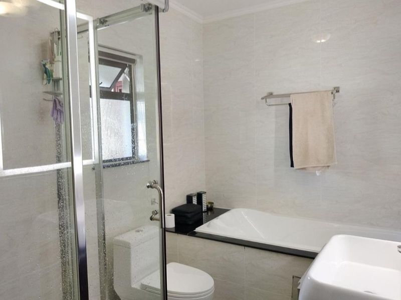 Modern bathroom featuring a glass-enclosed shower, built-in bathtub with granite surround, and neutral wall tiling.