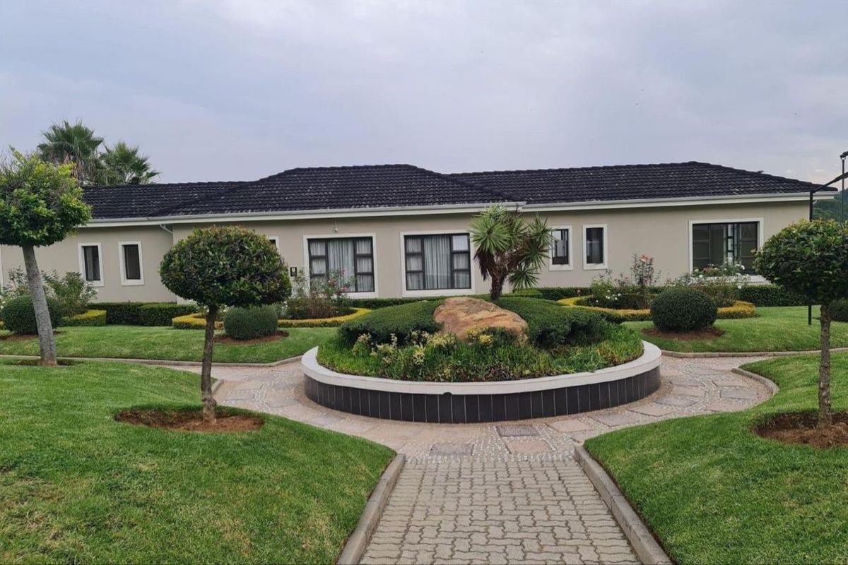 A well-maintained rear exterior view of the apartment building featuring a landscaped garden, paved pathways, and a central stone feature.