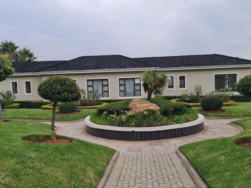 A well-maintained rear exterior view of the apartment building featuring a landscaped garden, paved pathways, and a central stone feature.