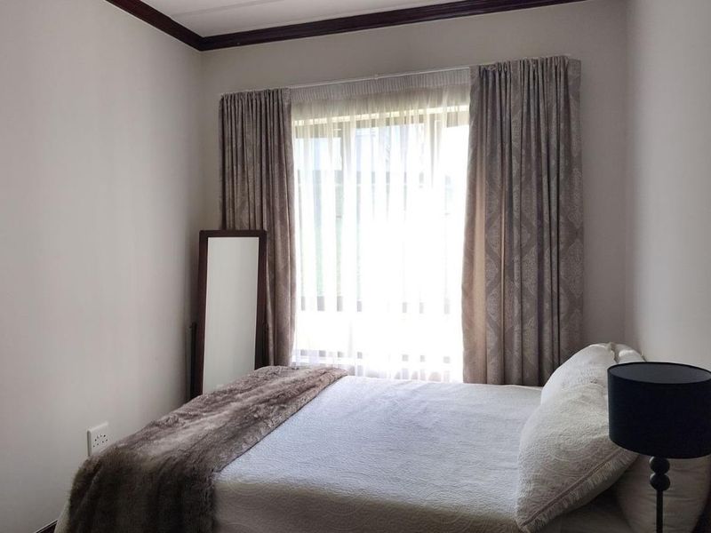 A cozy bedroom featuring neutral walls, crown molding, and large windows dressed with curtains, providing a comfortable and well-lit sleeping space.
