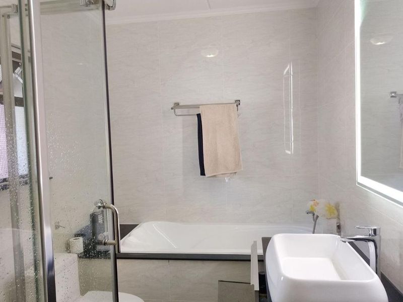 Modern bathroom featuring a built-in bathtub, glass-enclosed shower, vessel sink vanity, and an illuminated mirror with neutral wall tiling.