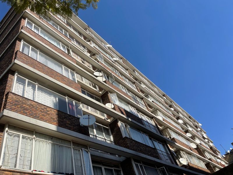 Low-angle exterior view of a multi-story brick apartment building featuring rows of sliding windows and mounted satellite dishes.
