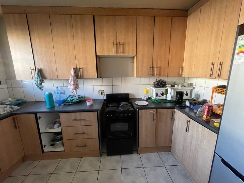 A functional kitchen featuring light wood-tone cabinetry, a tiled backsplash, and a freestanding electric stove, requiring some maintenance and cosmetic updates.