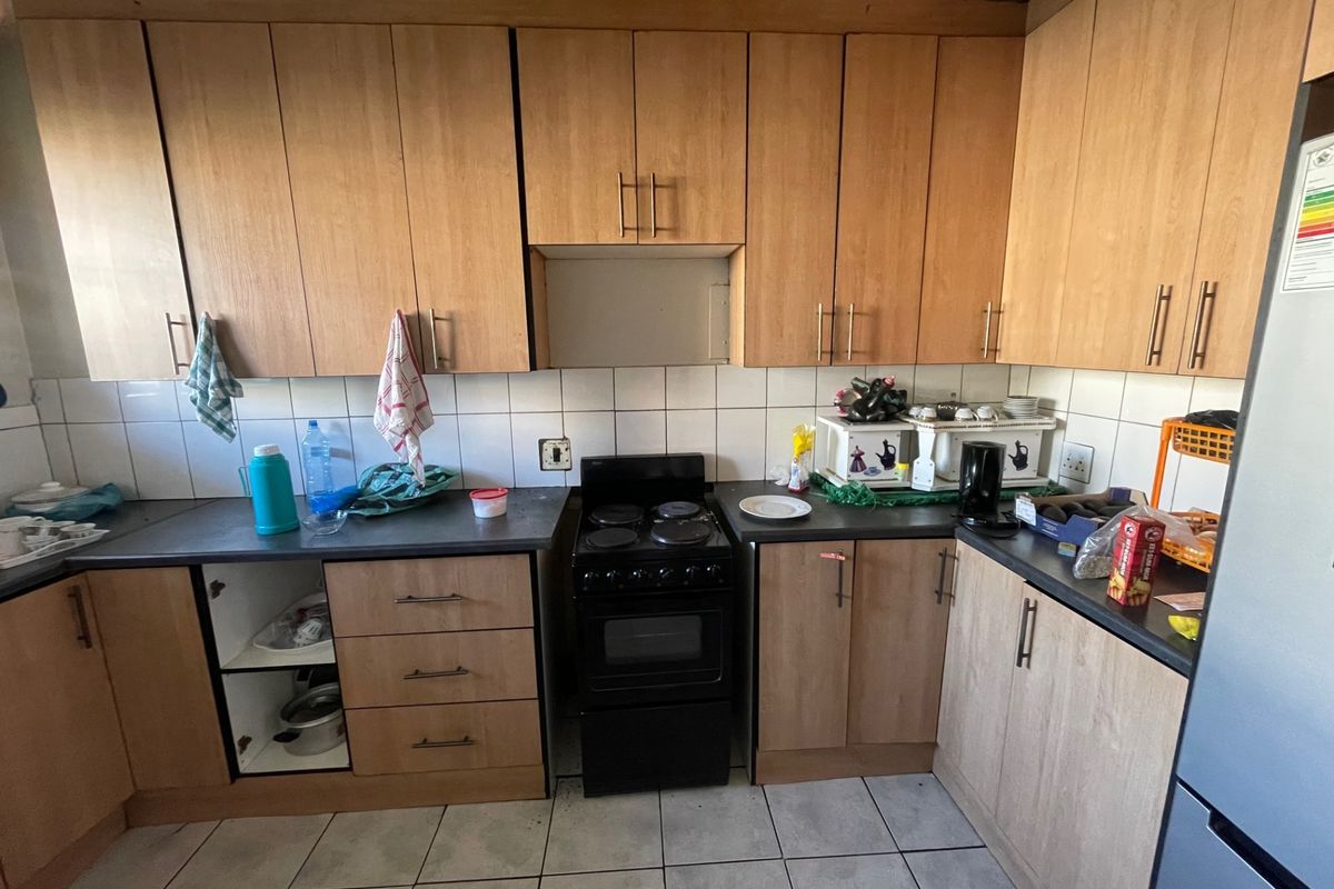 A functional kitchen featuring light wood-tone cabinetry, a tiled backsplash, and a freestanding electric stove, requiring some maintenance and cosmetic updates.