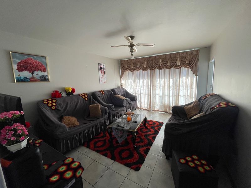 A living room featuring tiled flooring, a ceiling fan, and a large sliding glass door with decorative curtains.
