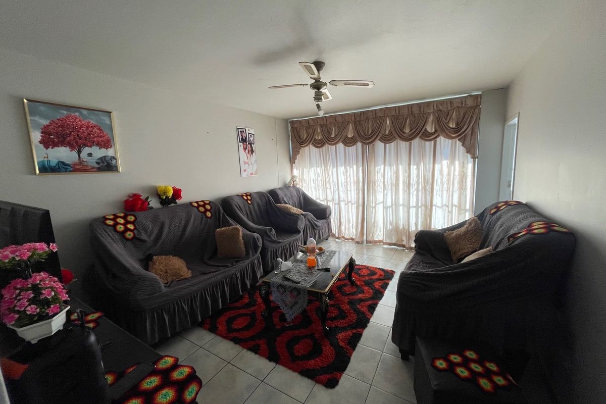 A living room featuring tiled flooring, a ceiling fan, and a large sliding glass door with decorative curtains.