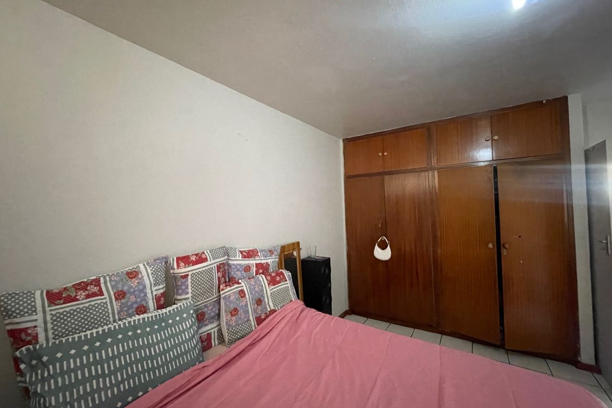 A bedroom featuring built-in wooden wardrobes and tiled flooring, offering a functional space with potential for cosmetic updates.