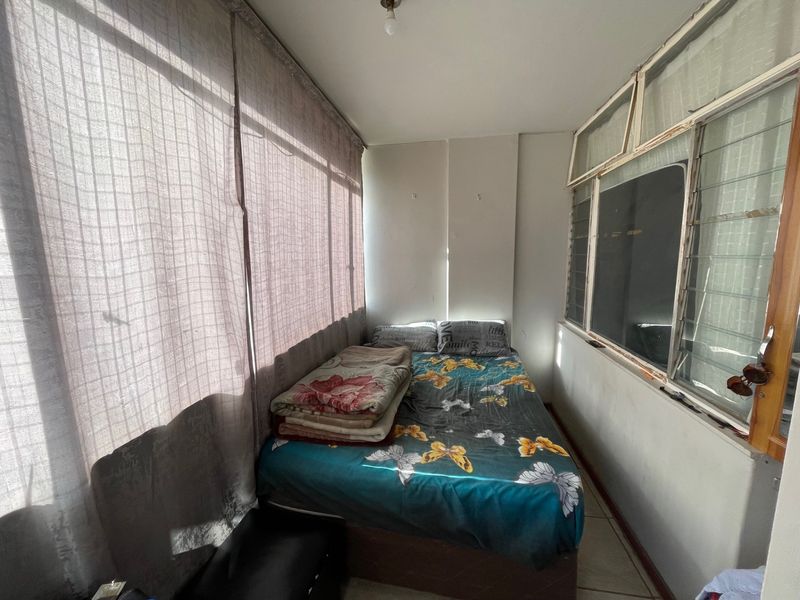 A compact bedroom featuring tiled flooring and louvered windows, offering a functional space that could benefit from cosmetic updates.