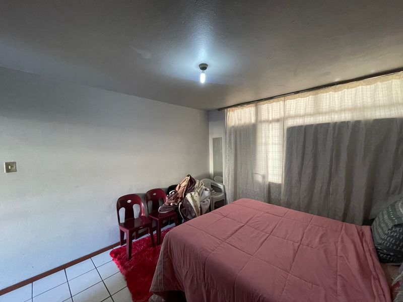 A bedroom featuring tiled flooring and a large window with curtain tracks, offering a functional space ready for cosmetic updates.