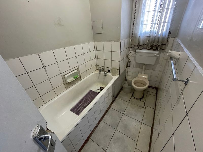 A dated bathroom featuring a built-in bathtub, toilet, and tiled finishes. The space requires renovation to address worn surfaces and outdated fixtures.
