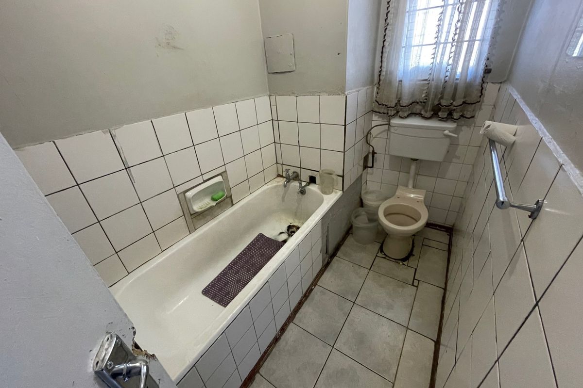 A dated bathroom featuring a built-in bathtub, toilet, and tiled finishes. The space requires renovation to address worn surfaces and outdated fixtures.