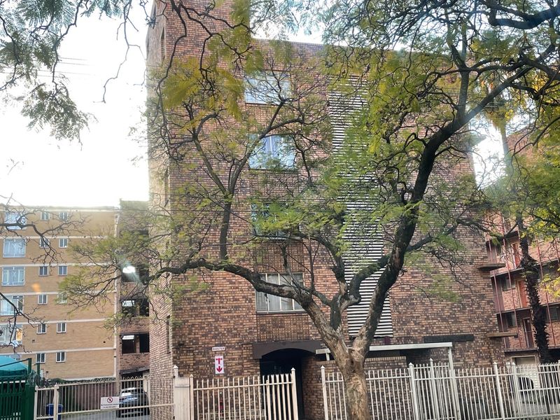 Exterior view of a multi-story face brick apartment building featuring secure metal perimeter fencing and mature trees.