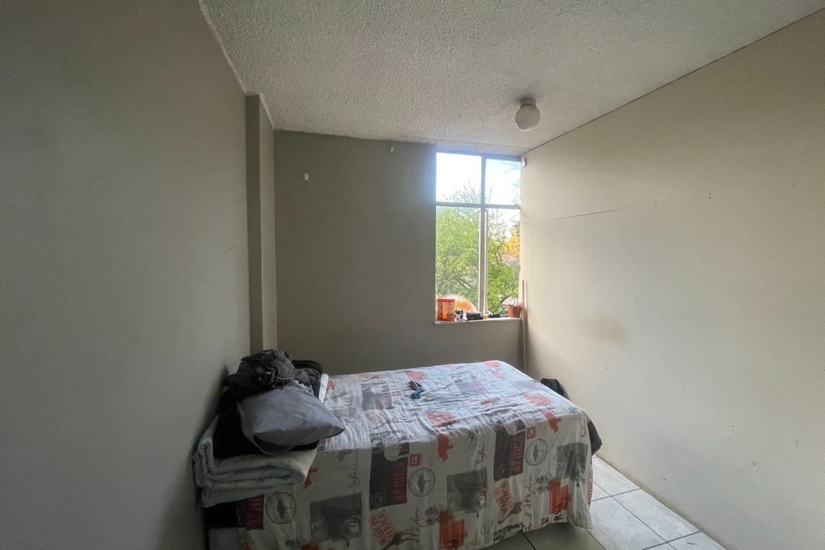 A simple bedroom featuring tiled flooring, a textured ceiling, and a large window providing natural light.