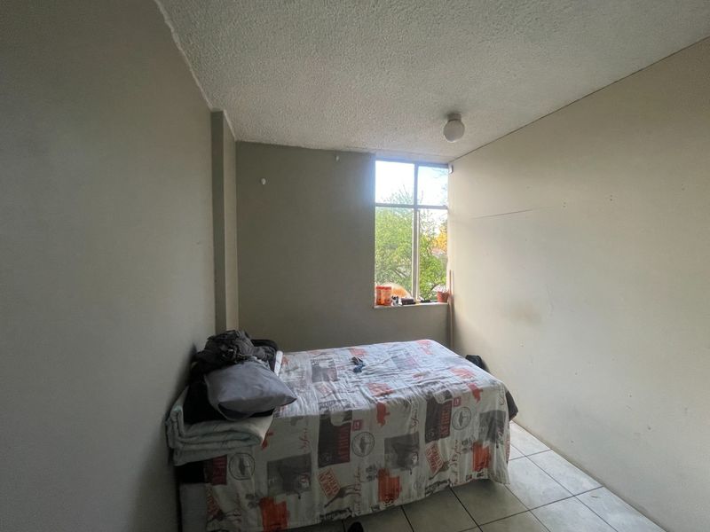 A simple bedroom featuring tiled flooring, a textured ceiling, and a large window providing natural light.