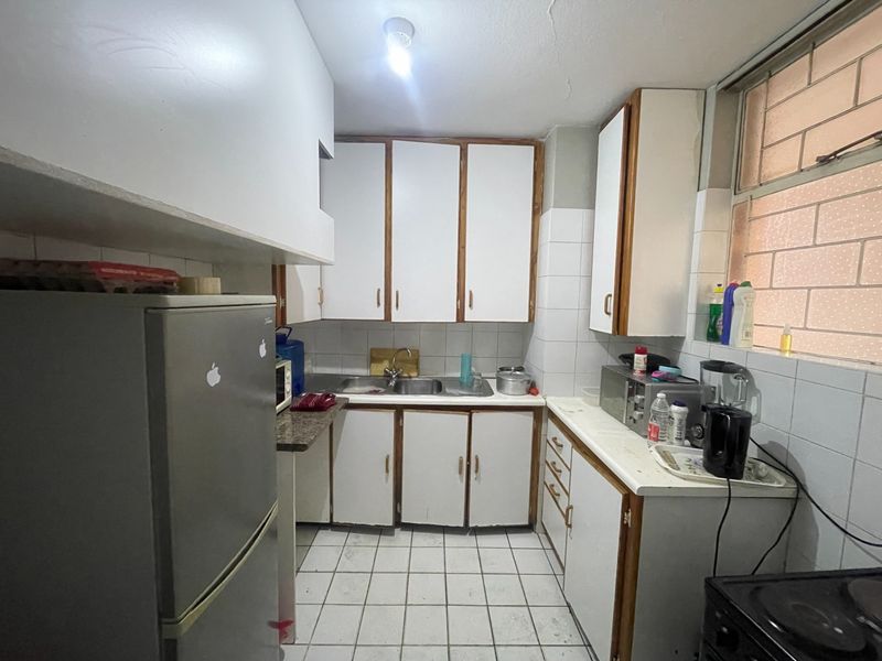 A functional kitchen featuring white cabinetry, tiled backsplash, and tiled flooring, offering a dated aesthetic with potential for modern renovation.