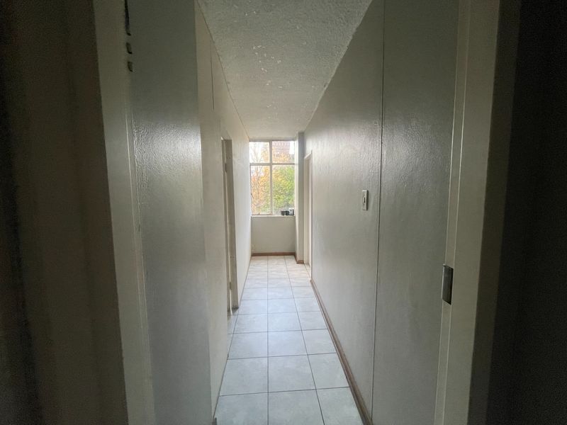 A vacant hallway featuring tiled flooring and a textured ceiling, leading towards a window with natural light.