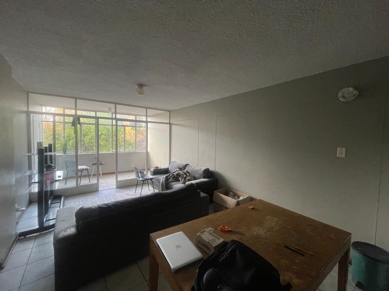 Open plan living area featuring tiled flooring and large aluminium framed glass doors leading to an attached balcony, providing natural light.