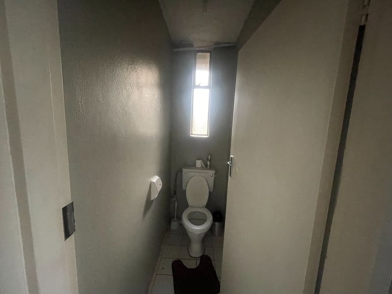 A compact, functional guest toilet featuring tiled flooring and a vertical window, currently in need of cosmetic updates and ceiling repairs.