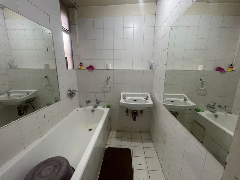A dated bathroom featuring a bathtub, wall-mounted basin, and full-height wall tiling, requiring cosmetic updates to improve its overall condition and appeal.