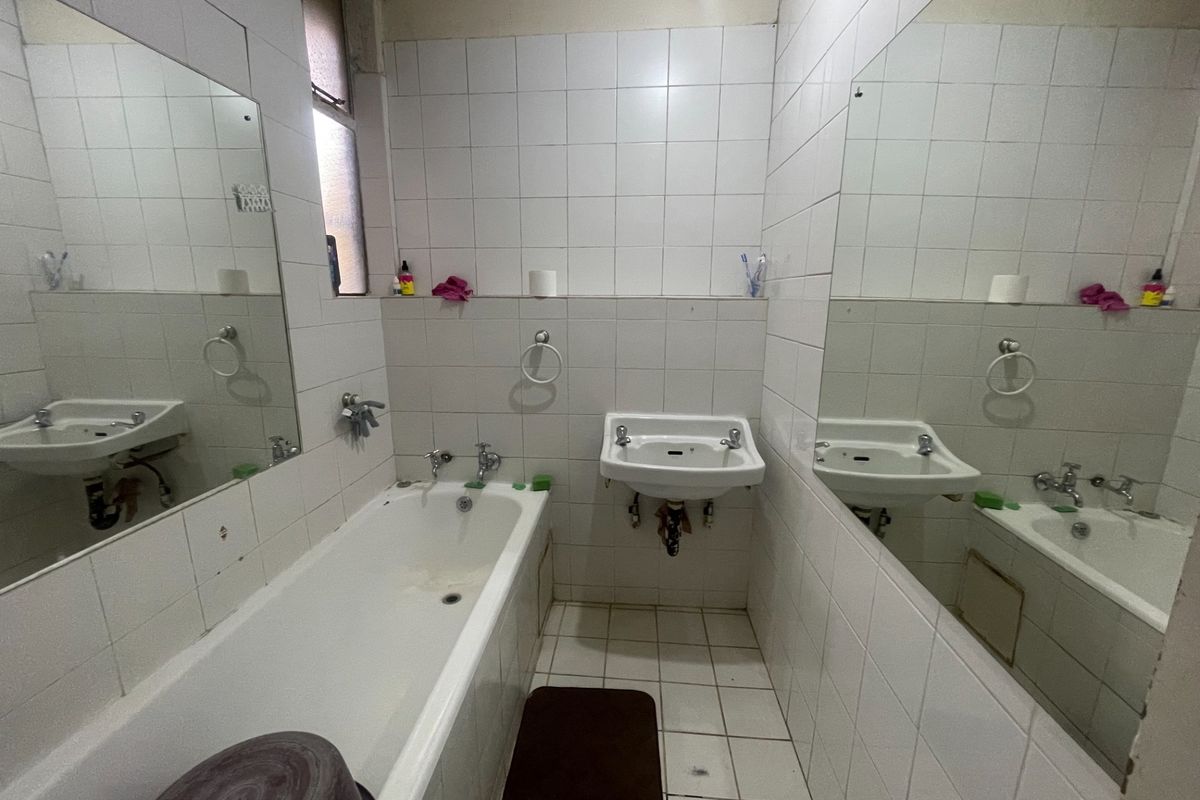 A dated bathroom featuring a bathtub, wall-mounted basin, and full-height wall tiling, requiring cosmetic updates to improve its overall condition and appeal.