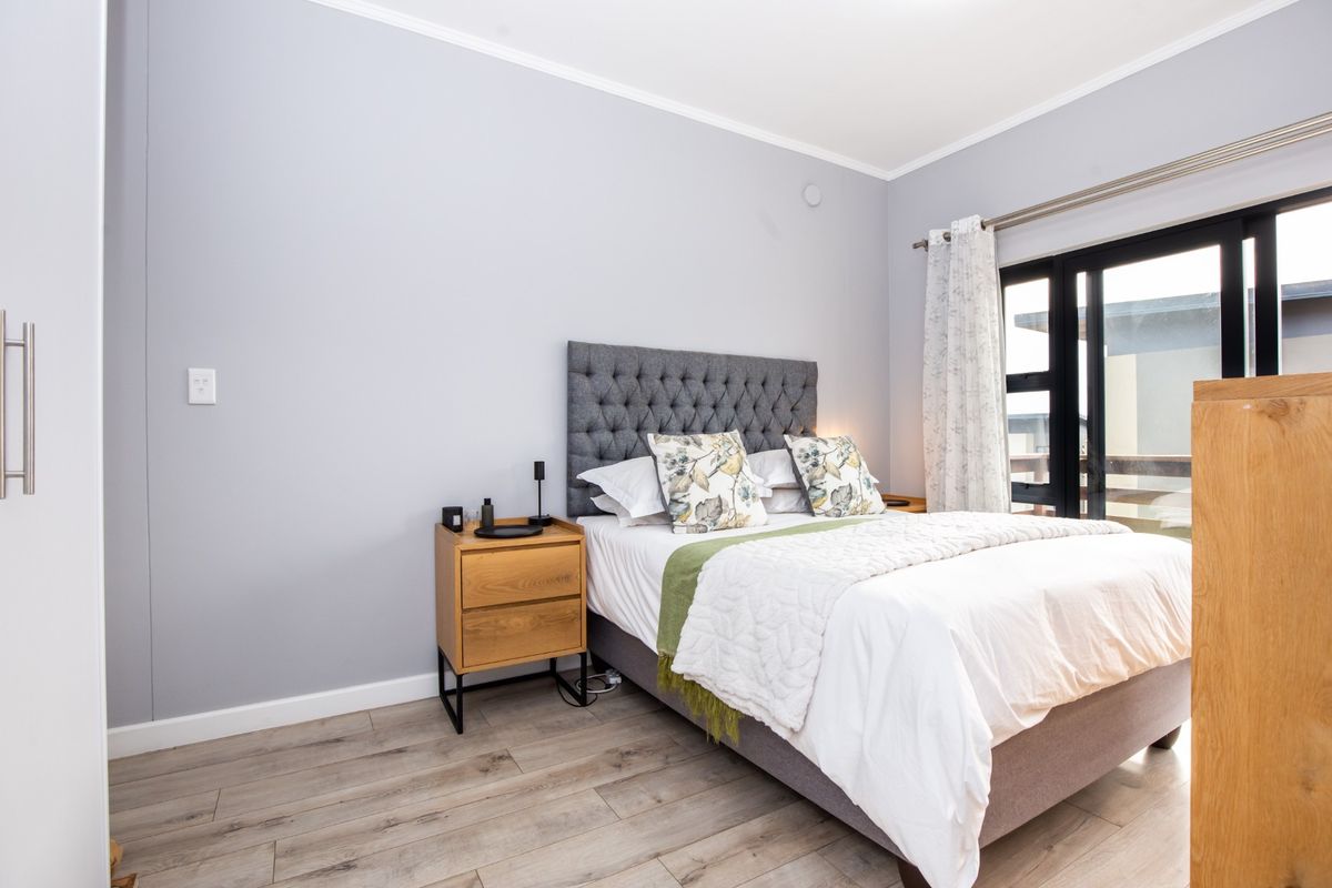 A well-maintained bedroom featuring light-toned laminate flooring, neutral walls, and a sliding glass door providing access to an outdoor area.