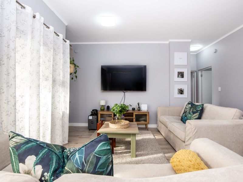 A well-maintained living room featuring laminate flooring, neutral wall tones, and a large sliding glass door providing natural light.