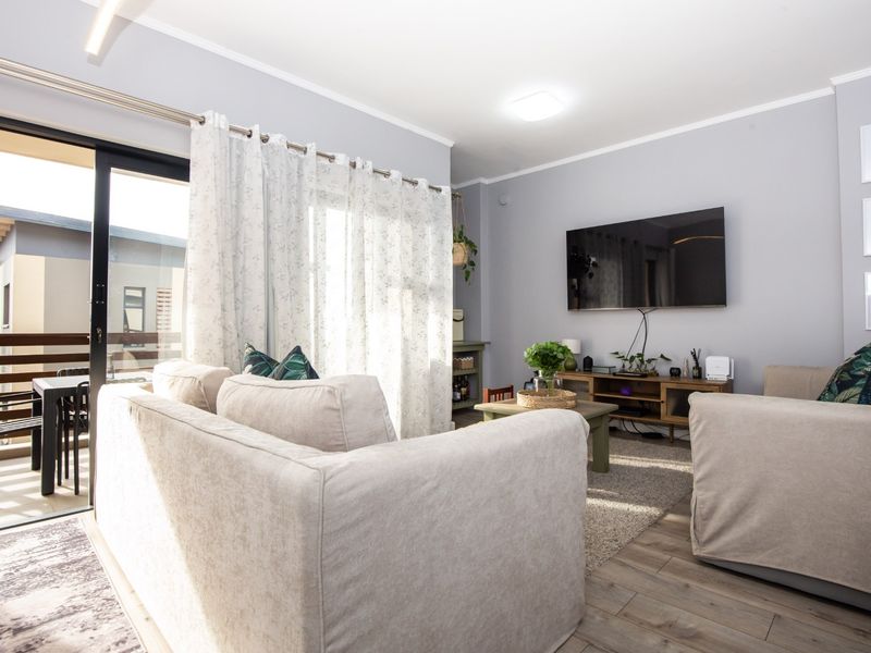A bright and well-maintained living room featuring laminate flooring, coving, and a large sliding glass door providing access to an outdoor balcony area.