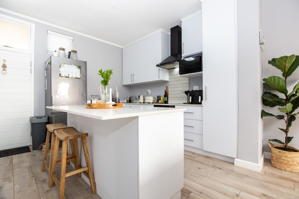Modern kitchen featuring a central island, sleek white cabinetry, built-in appliances, and light wood-look laminate flooring.