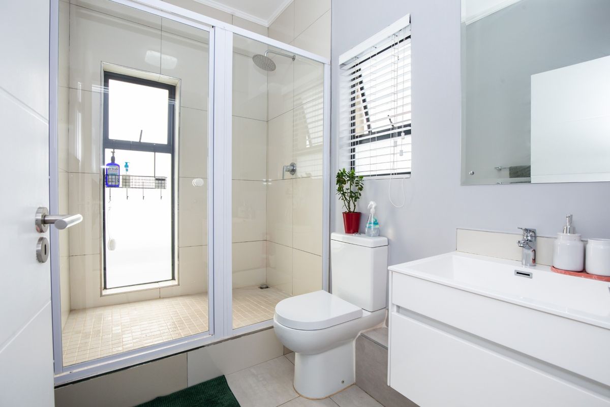 Modern bathroom featuring a glass-enclosed shower with rain shower head, wall-mounted toilet, and a sleek white vanity cabinet with basin.