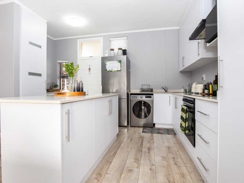 Modern kitchen featuring white cabinetry, a central island, integrated appliances, and light wood-look laminate flooring in a clean, well-maintained space.