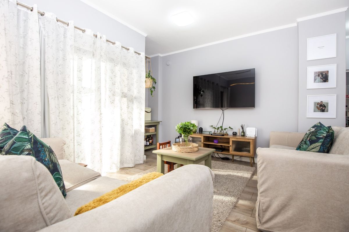 A bright and well-maintained living room featuring laminate flooring, neutral wall tones, and a large sliding glass door providing ample natural light.