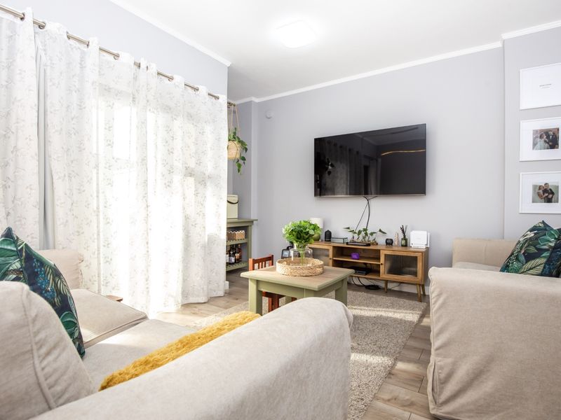 A bright and well-maintained living room featuring laminate flooring, neutral wall tones, and a large sliding glass door providing ample natural light.