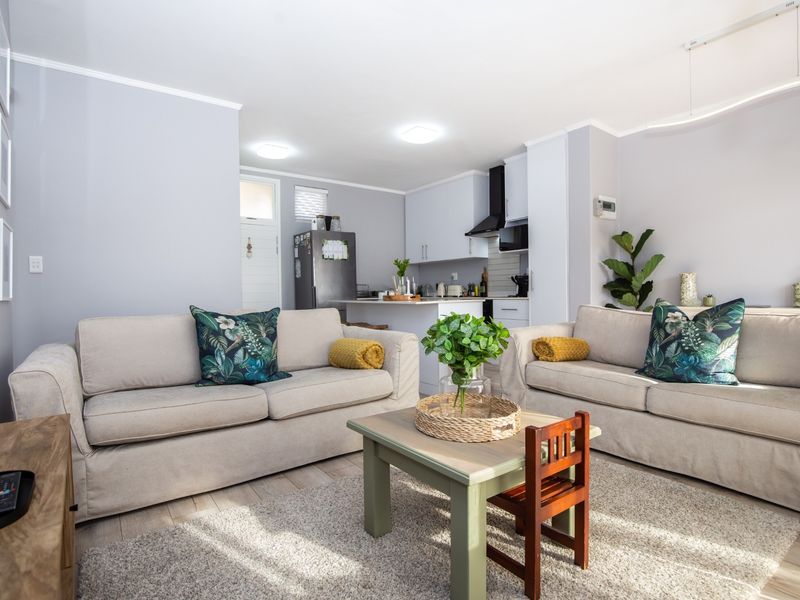 An open-plan living area featuring a modern kitchen with white cabinetry, extractor fan, and light laminate flooring throughout the space.