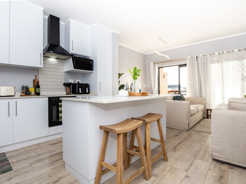 Modern open-plan kitchen and living area featuring a central island, sleek cabinetry, built-in appliances, and light wood-look flooring with access to a balcony.