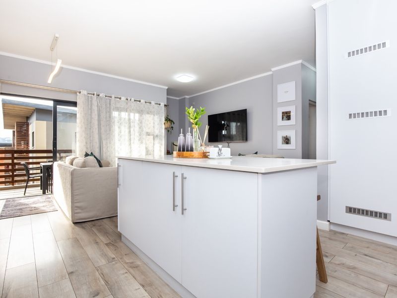 Modern open-plan living area featuring a central kitchen island, light laminate flooring, and seamless access to an outdoor balcony through sliding glass doors.